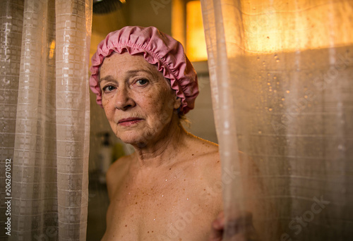 Seniorin um die 70 mit Duschhaube schaut hinter dem Duschvorhang hervor – Körperpflege und Altern im Alltag