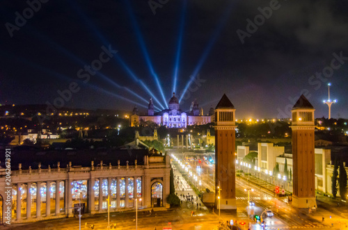 Fotografía « Vue nocturne de la place d’Espagne à Barcelone, illuminée par ses tours emblématiques et ses faisceaux lumineux, symbole du patrimoine urbain et de l’attractivité culturelle catalane