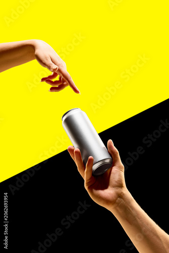 Fotografie Blank silver aluminum can passed between two hands on yellow and black geometric background
