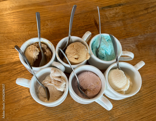 Assorted ice cream balls in white cups on a wooden table.
