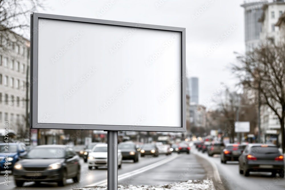 Fototapeta premium Blank billboard in a busy city street with blurred traffic and buildings, ready for advertisement.