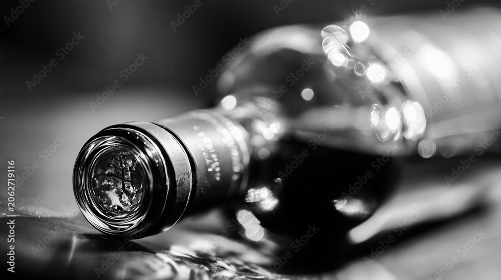 Obraz premium Close up black and white shot of a glass wine bottle lying on its side, showcasing reflections and bokeh