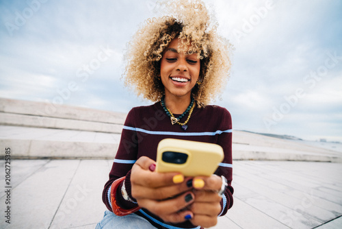 Young woman smiling while using smartphone outdoors