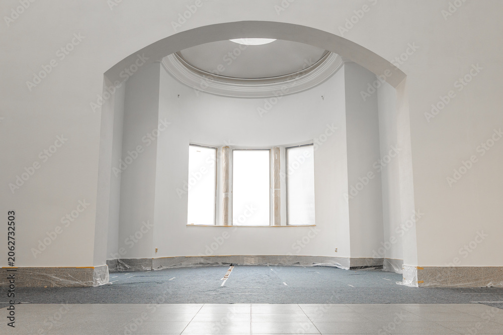 Obraz premium Empty room in an old building in the ground floor. Renovation work like painting the wall with white color. Construction site with masked flooring and a fleece cover.