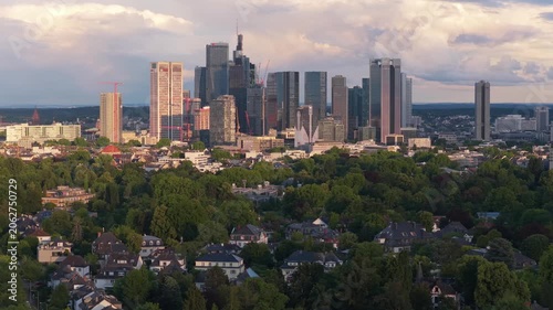 Frankfurt skyline glowing during golden hour sunset with modern skyscrapers and residential buildings surrounded by green trees, metropolitan urban landscape