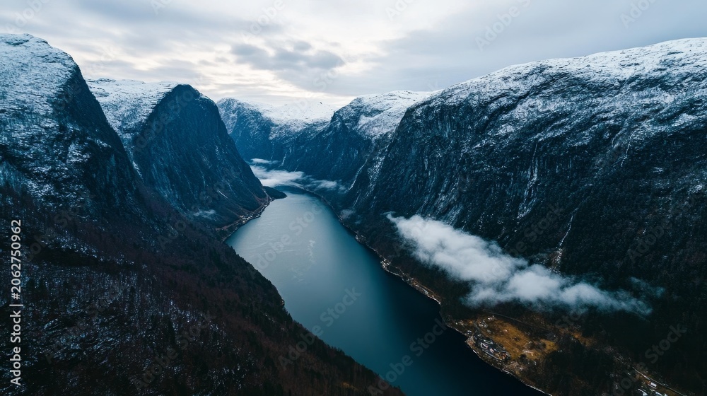 Obraz premium Winter fjord with steep, snow-capped rocky mountains and wispy clouds over calm water