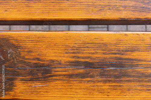 Wooden bench close-up showing textured surface and grain patterns in an outdoor setting during daytime