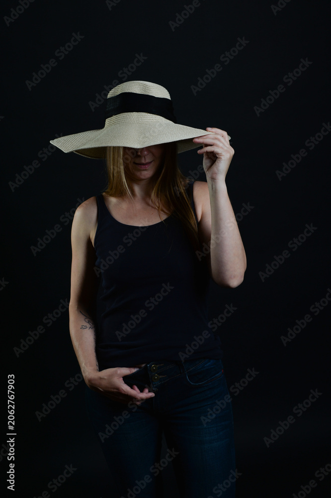 Fototapeta premium Frau mit großem Sonnenhut in dunkler Low-Key-Beleuchtung. Elegantes Lifestyle-Motiv für Sommer, Mode, Anonymität, Selbstbewusstsein, Weiblichkeit und stilvolle Porträts.