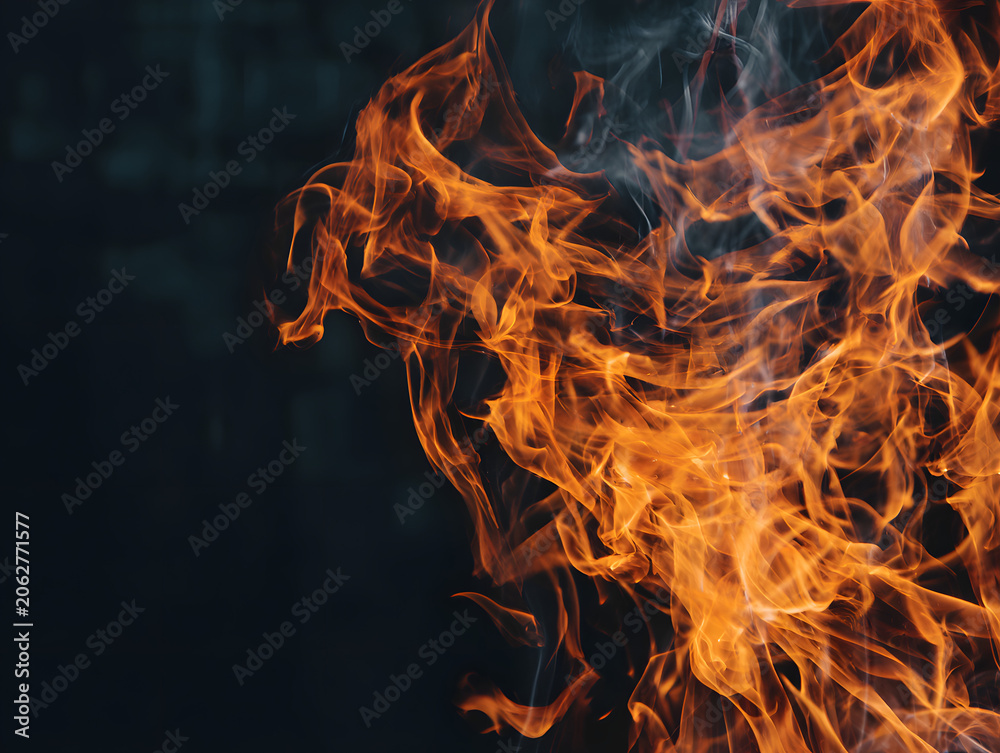 Fototapeta premium Macro detail of dancing orange fire flames against dark moody background with smoke wisps.