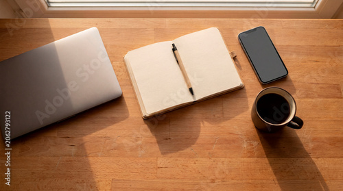 Flat lay of laptop blank notebook smartphone and coffee on warm wooden desk