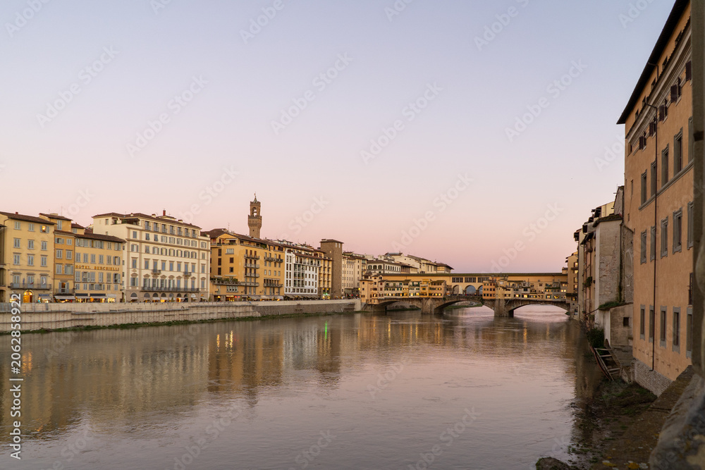Fototapeta premium The iconic Ponte Vecchio bridge spans the Arno River in Florence, Italy, illuminated by the soft glow of twilight
