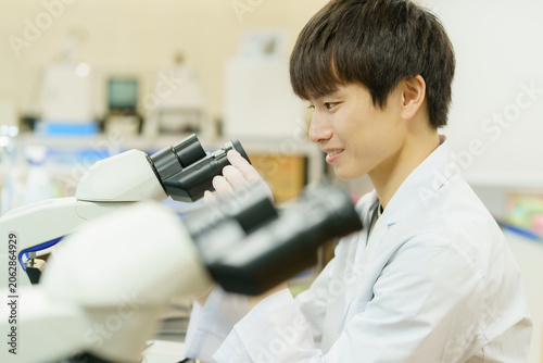 顕微鏡で作業をする白衣を着た若い日本人男性　実験　研究　開発　勉強　
撮影協力：学校法人電波学園 東京電子専門学校
