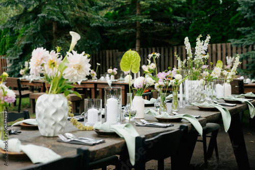 Close-up of elegant outdoor wedding table with dahlia and calla lily flowers in white geometric vase beside pillar candles and sage linen