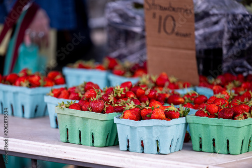 Obraz na plátně Pint baskets of ripe strawberries sit behind a handwritten price sign at a farmers market stand, the simple economics of buying close to the source