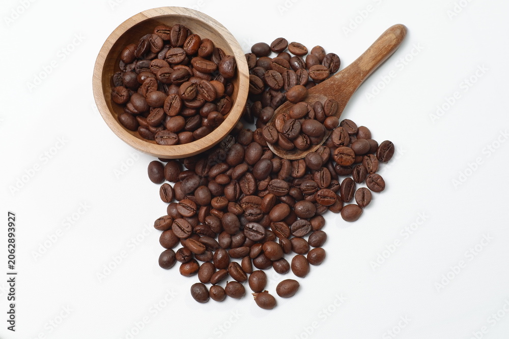Fototapeta premium A pile of roasted coffee beans with a bowl and a small wooden spoon on a clean white background. Perfect for design elements, organic culinary themes, and the coffee industry.
