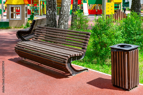 Empty wooden bench and trash can on a children's playground.