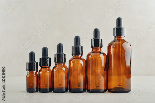 Amber glass dropper bottles of different sizes arranged in ascending order from smallest to largest on light background.