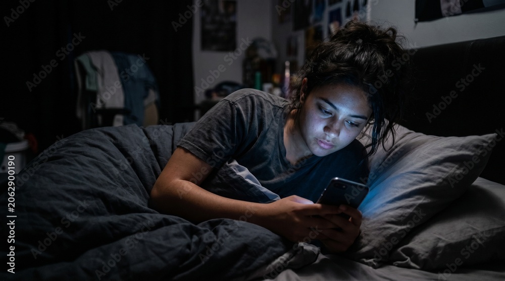 Obraz premium Young woman using smartphone in bed at night with dark background, lifestyle photography concept of social media addiction, digital communication, insomnia, and late night technology use at home.