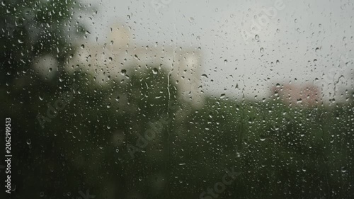 Large raindrops on the window during the rain against the background of the city