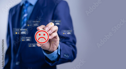 Obraz na plátne Businessman holding sad face icon with low customer rating and negative reviews