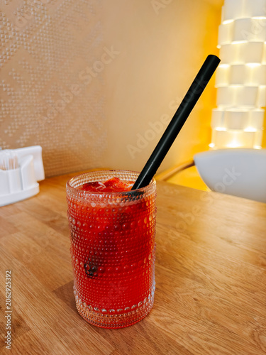 Refreshing red beverage with ice and a black straw on a wooden table