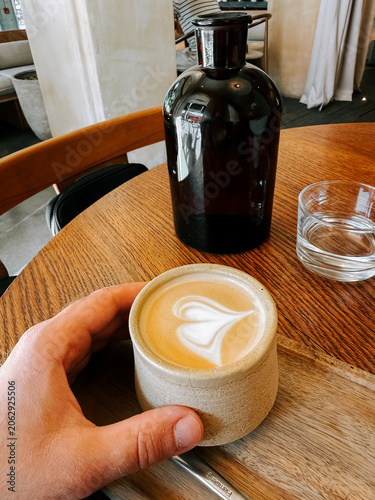 Hand holding coffee cup with beautiful latte art on wooden table