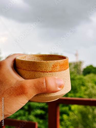 Person holds ceramic cup with hot drink on balcony during cloudy day