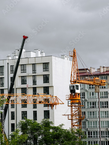 Mobile crane lifts section for tower crane assembly near modern city buildings