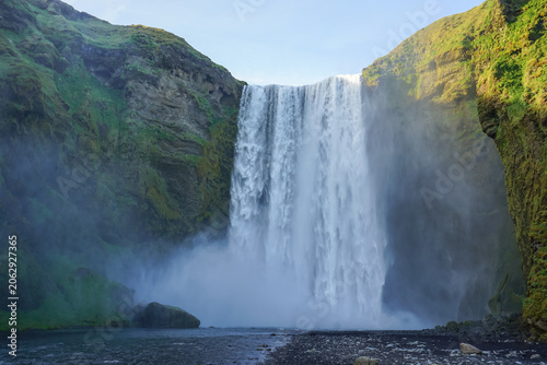 Quadro su tela A powerful waterfall cascades down a steep cliff into a misty pool surrounded by