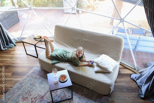 Cozy glamping lifestyle with a woman resting indoors, using a mobile phone in a modern geodesic dome accommodation.