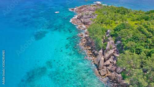 Fotografie High-angle drone view of Little Sister Island, Seychelles, showcasing an excursion boat anchored in turquoise water next to a white sandy beach and lush green forest