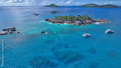Valokuva Stunning drone shot of Cocos Island, Seychelles, showing a luxury catamaran and boat anchored in clear turquoise water surrounded by granite rocks and coral reefs