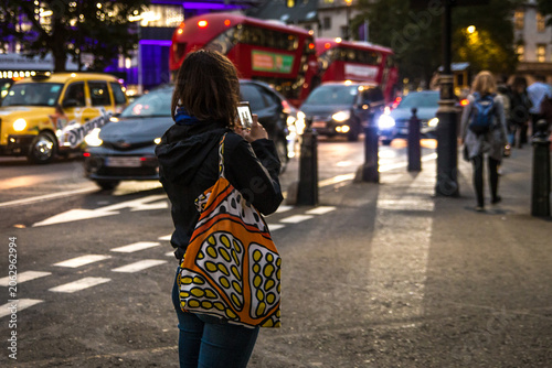 Canvas-taulu young woman walking on the street taking a picture with phone