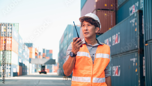 Bild auf Leinwand Asian worker safety vest hard hat walkie talkie shipping container cargo port lo
