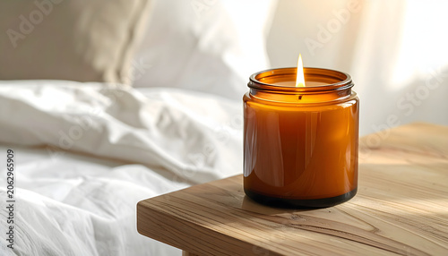 Lighted scented candle in amber glass jar on wooden bedside table