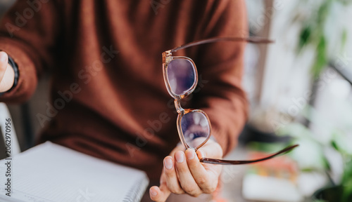 Close-up of a person holding eyeglasses over a notebook on a desk. Casual office scene showing eyewear and hands during a business planning moment.