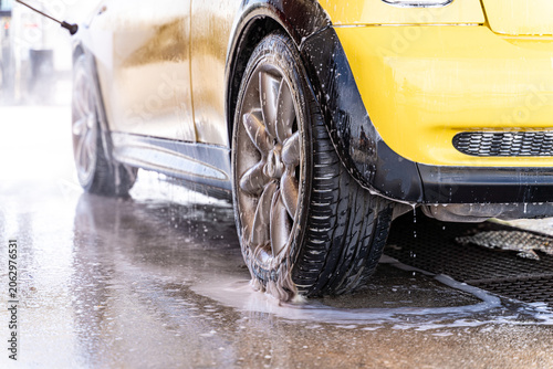 Close-up of a yellow car tire covered in soap foam during a car wash. Focus on texture and water, conveying concepts of automobile maintenance and environmental protection.