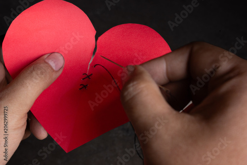 Foto Close up of hands sewing a torn heart-shaped paper together, representing forgiveness, reconciliation, healing emotional wounds, rebuilding relationships, and starting over concept