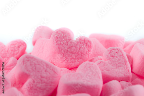 Pile of pink heart shaped marshmallows on a white background. Close-up