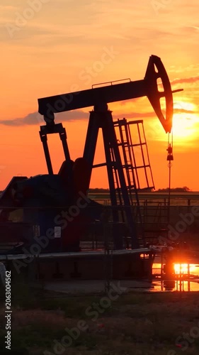 Silhouette of oil pump jack against a colorful beautiful sky with glowing clouds at sunset
