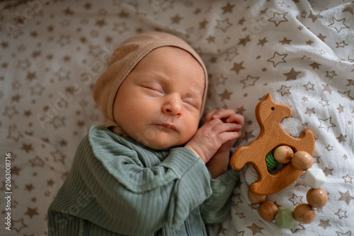 Newborn infant sleeping soundly in a bassinet or crib, hands gently folded, wearing a cozy green outfit and bonnet, with a natural wooden toy beside the baby, displaying early childhood and comfort
