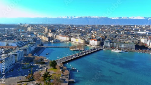 4K aerial drone footage over Geneva, Switzerland - Lake Léman, Pont du Mont-Blanc, Rhône River outlet, lakefront quays, luxury hotels, paddle steamer, and snow-capped Alps on the horizon.