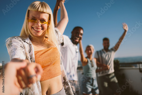 Young woman pulling hand to join diverse friends dancing