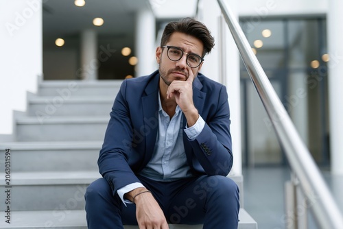 Man in a suit sits on steps in a modern building while deep in thought during a workday