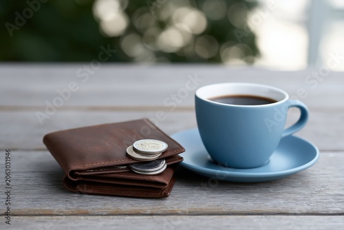 Coffee and wallet with coins placed on a wooden table outdoors in a sunny setting