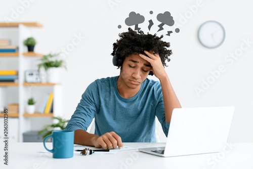 Young person sitting at desk showing signs of stress while working on a laptop during the day
