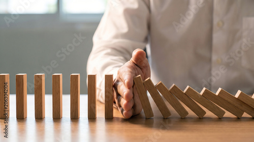 A professional businessman uses his hand to stop falling wooden dominoes representing effective risk management and crisis prevention