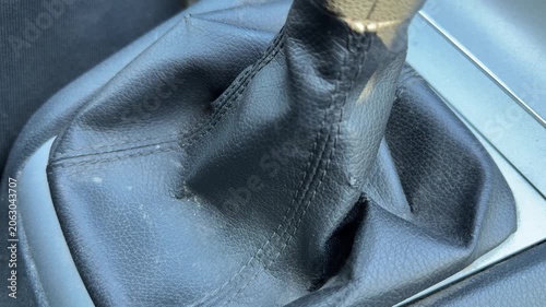 Driver shifts gears with a manual transmission lever inside a car, close-up of black leather gear boot, driving control, automotive operation, vehicle interior.