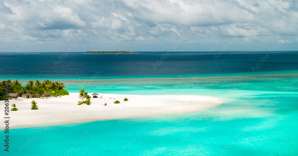 Fototapeta premium Aerial view of a Maldivian atoll sandbank with few palms and shallow turquoise lagoons, deep cobalt waters, tiny uninhabited islet, distant reef line, and bright daylight