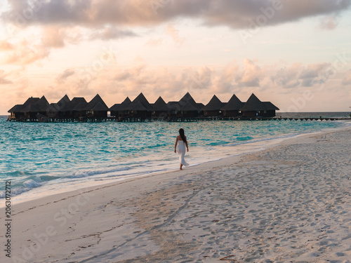 Foto A woman in a white dress walks along a pale sandy shore at sunset in Maldives